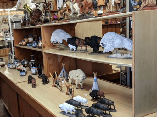 A display of various decorative figurines, including bison, pottery, and miniature teepees on wooden shelves.