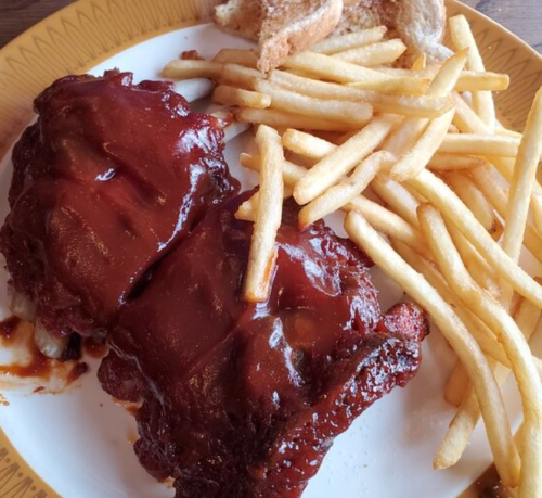 A plate with two barbecue ribs, golden fries, and a slice of toasted bread.