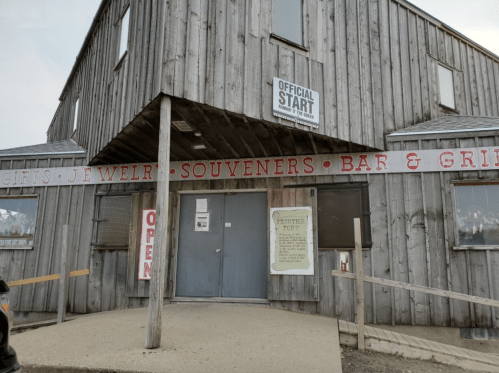 A rustic wooden building with signs for gifts, jewelry, souvenirs, and a bar, marked as the "Official Start."