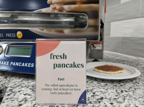 Sign for fresh pancakes with a humorous note about the robot apocalypse, next to a plate of pancakes.