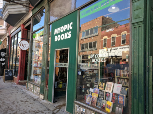 Exterior of Myopic Books, a cozy bookstore with large windows displaying books, located on a city street.