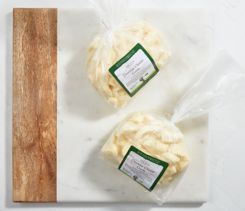 Two bags of cheddar cheese curds on a marble and wood cutting board.