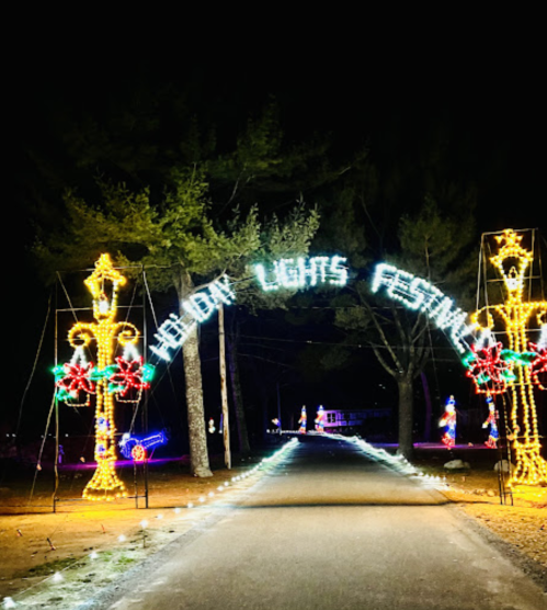 A festive archway reading "Holiday Lights Festival" illuminated by colorful lights, set along a dark pathway.