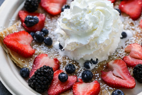 A delicious crepe topped with whipped cream, strawberries, blueberries, and blackberries, dusted with powdered sugar.