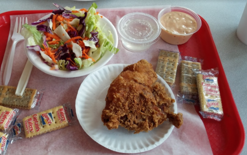 A tray with fried chicken, a side salad, dipping sauce, and crackers.