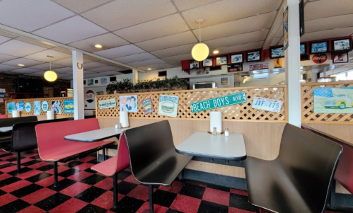 A retro diner interior with red and black checkered floors, colorful wall signs, and cozy seating booths.