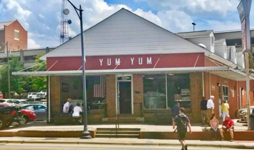 A red and white building with "YUM YUM" signage, featuring an American flag, with people walking outside.