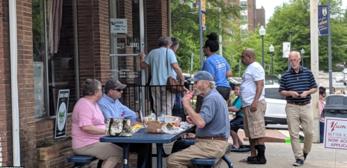 A group of people dining outside a restaurant, with some standing and others seated at a table.