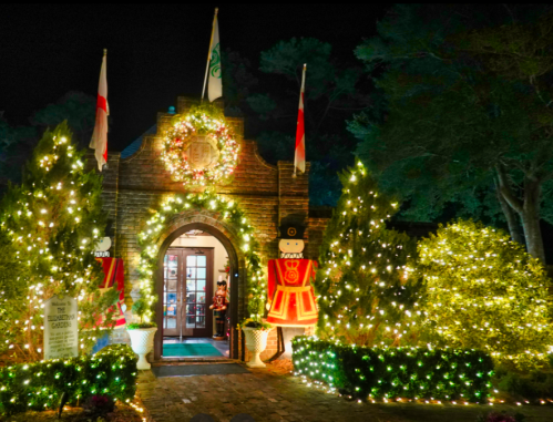 A festive entrance adorned with lights, wreaths, and nutcracker decorations, surrounded by greenery at night.