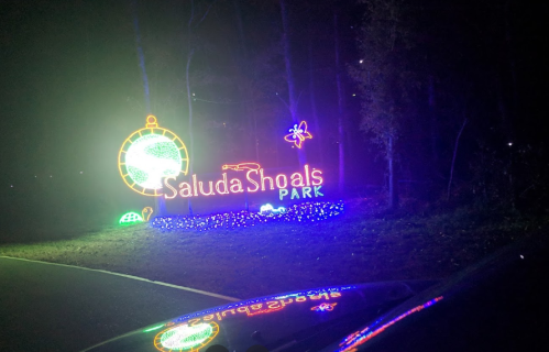 Brightly lit sign for Saluda Shoals Park, surrounded by fog and colorful lights at night.