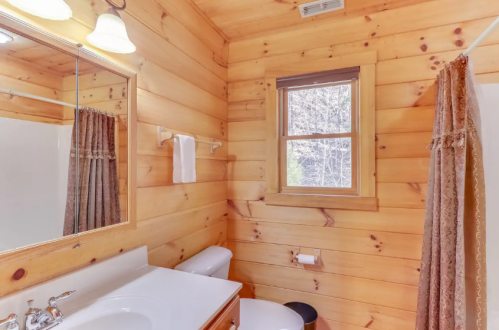 Cozy wooden bathroom with a mirror, sink, toilet, and a window letting in natural light.