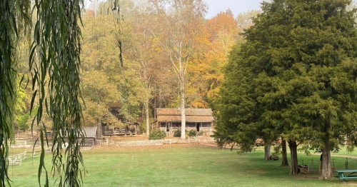 A serene landscape featuring a rustic cabin surrounded by trees and autumn foliage.