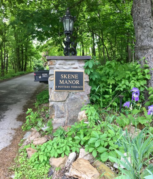Sign for Skene Manor at the entrance, surrounded by greenery and flowers, with a lamp post nearby.