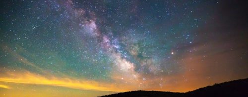 A stunning night sky filled with stars and the Milky Way, illuminated by soft clouds and a distant horizon.