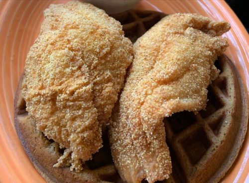 Two pieces of golden fried chicken served on a waffle, with a side of dipping sauce.