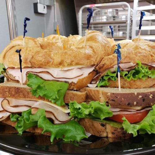 A platter of stacked sandwiches with croissant and bread, filled with turkey, lettuce, and tomato, garnished with toothpicks.