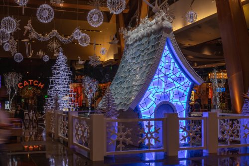 A festive display featuring a blue-lit, snow-covered house surrounded by snowflake decorations and holiday lights.