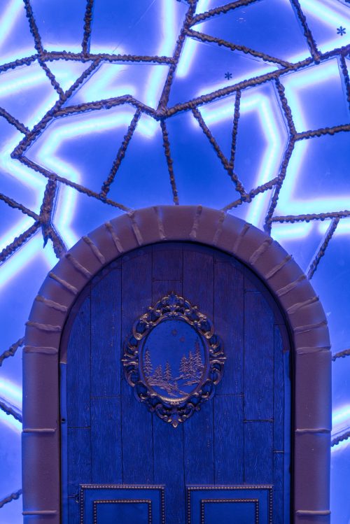 A decorative blue door with a circular design, set against a starry, illuminated blue wall.