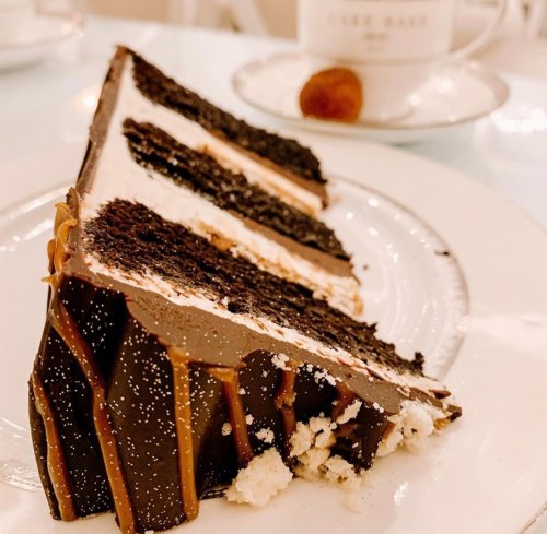 A slice of rich chocolate cake with layers of cream and drizzled caramel, served on a white plate.