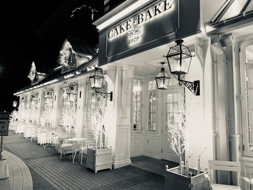 A charming cake shop at night, illuminated with white lights and lanterns, featuring outdoor seating and festive decor.