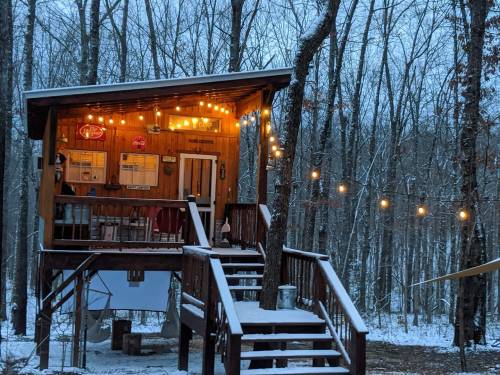 A cozy wooden cabin in a snowy forest, adorned with string lights and surrounded by trees.