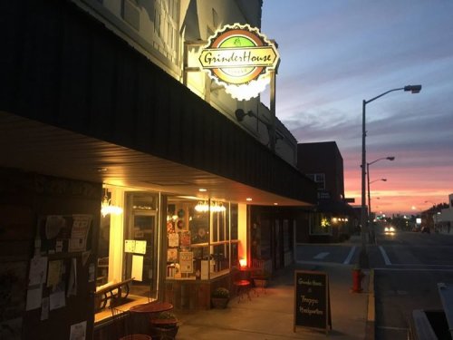 A cozy storefront with a sign reading "Garden House" illuminated at dusk, with a colorful sunset in the background.