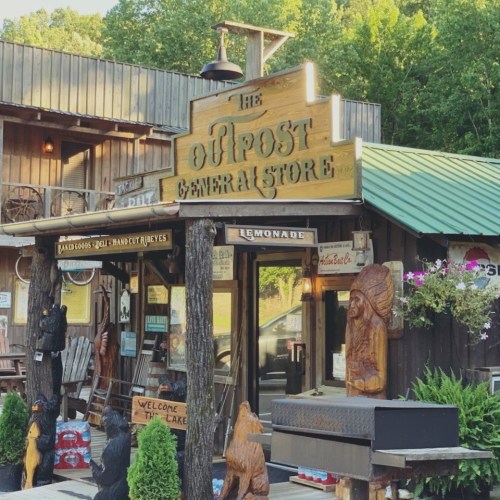 A rustic general store with wooden signage, surrounded by carved bear statues and greenery.