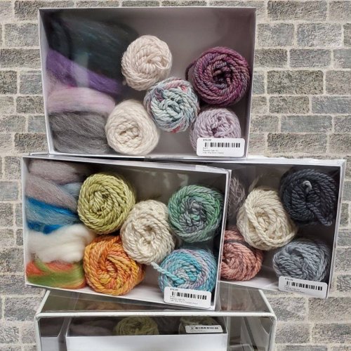 Three boxes of colorful yarn and fiber, neatly arranged, showcasing various textures and shades against a brick background.