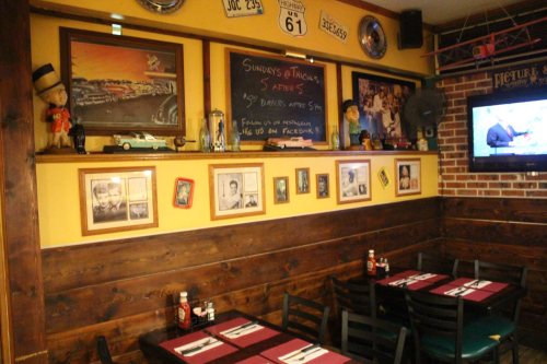 Cozy restaurant interior with wooden walls, vintage decor, and tables set for dining. A chalkboard lists specials.