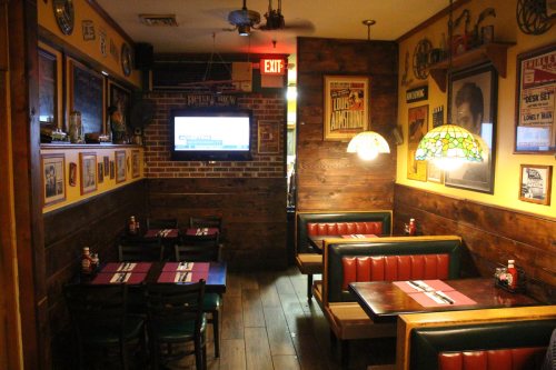 Cozy restaurant interior with wooden walls, booths, and vintage decor, featuring a TV and stained glass lamps.