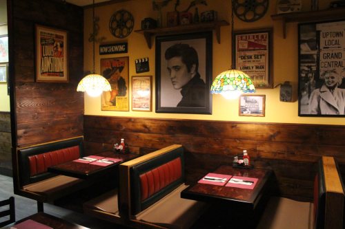 Cozy restaurant interior with vintage decor, featuring a large Elvis portrait and stained glass lamps over booth seating.