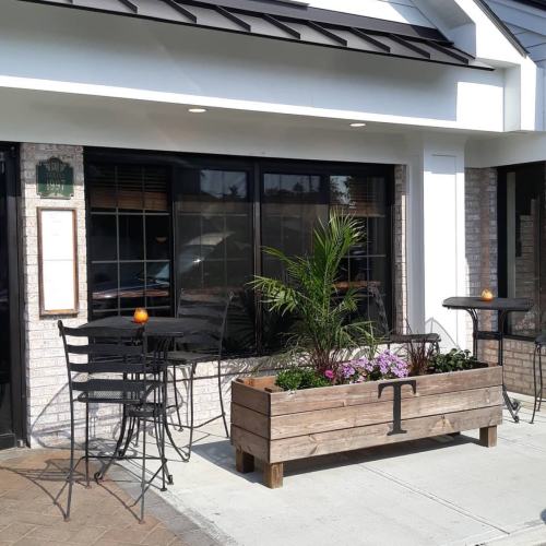 Exterior of a restaurant featuring a wooden planter, outdoor seating, and large windows.