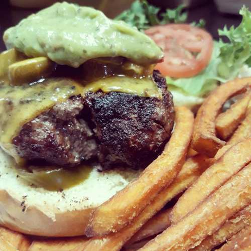 A juicy burger topped with guacamole and cheese, served with sweet potato fries and fresh lettuce and tomato.