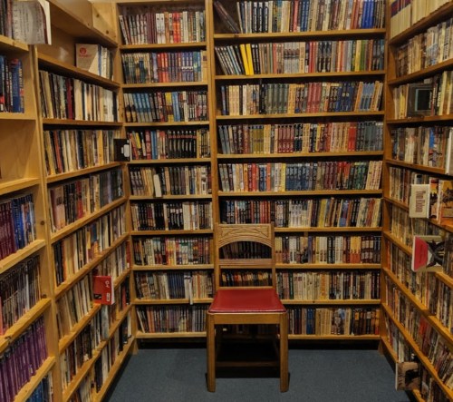 A cozy corner of a library with wooden shelves filled with books and a single red chair in the center.