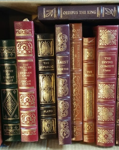 A collection of classic literature books with ornate covers, including titles by Frost, Wilde, Plato, and Goethe.