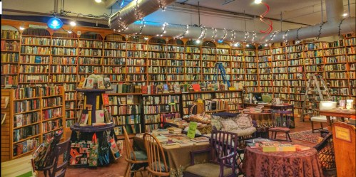 Cozy bookstore interior filled with bookshelves, tables, and chairs, adorned with string lights and a ladder.