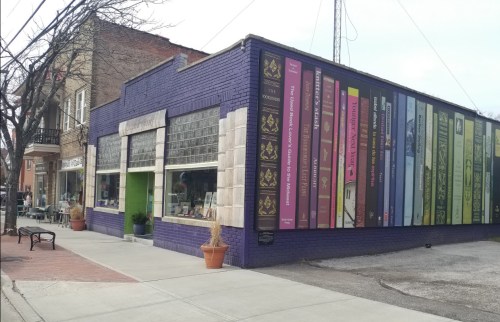 A colorful bookstore exterior featuring large book spines painted on the wall, with a sidewalk and nearby buildings.