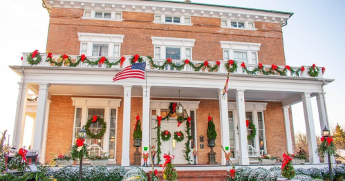 A festive brick house decorated with wreaths and ribbons, featuring an American flag and a snowy landscape.