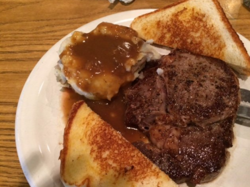 A plate with a grilled steak, mashed potatoes with gravy, and two slices of toasted bread.