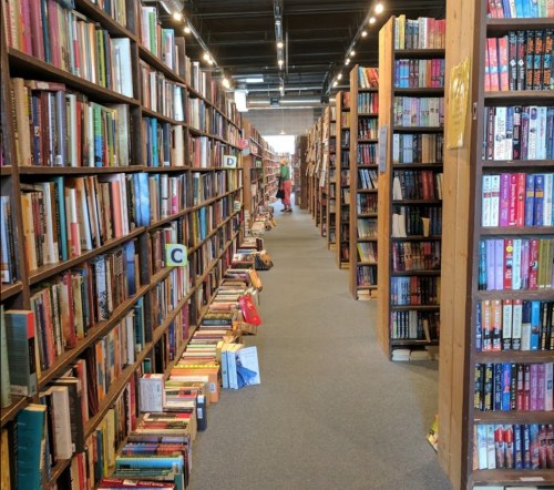 A spacious bookstore aisle lined with tall wooden shelves filled with colorful books.