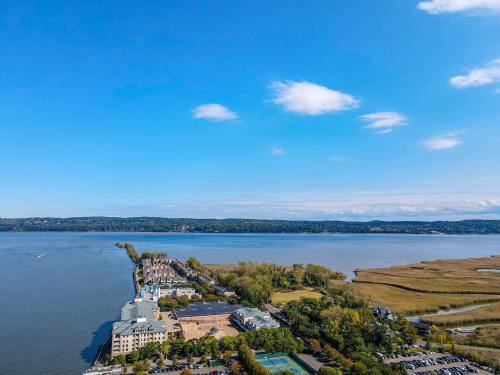 Aerial view of a river with a shoreline, buildings, and green areas under a clear blue sky.