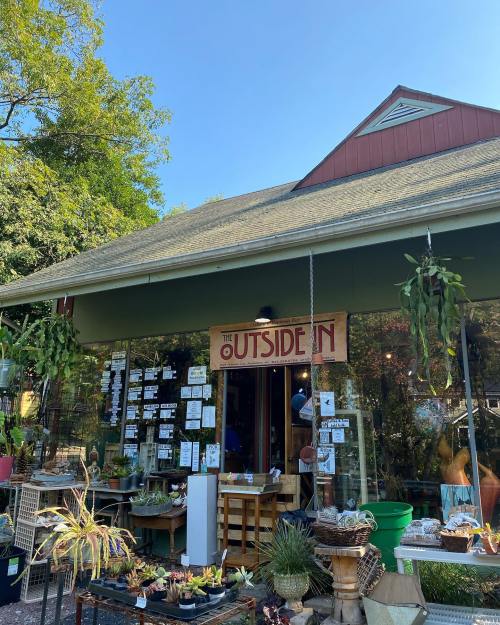 A charming garden shop with a sign reading "The Outside In," featuring plants and greenery outside.