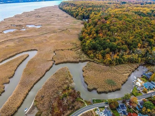 Aerial view of a river winding through marshland and colorful autumn foliage along the shore.