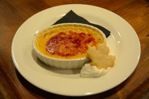A creamy crème brûlée topped with caramelized sugar, served with a cookie and whipped cream on a white plate.
