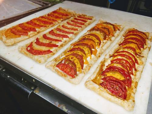 Three rectangular tarts topped with layers of colorful sliced tomatoes on a white cutting board.
