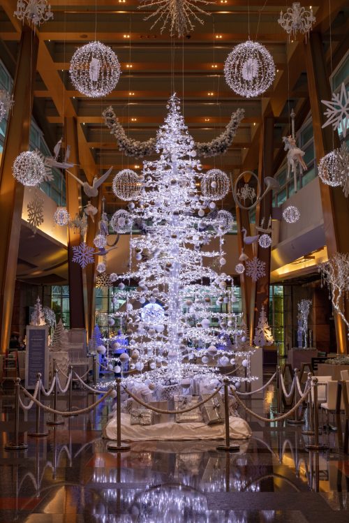 A beautifully decorated lobby featuring a large, illuminated Christmas tree surrounded by snowflake ornaments and festive decor.