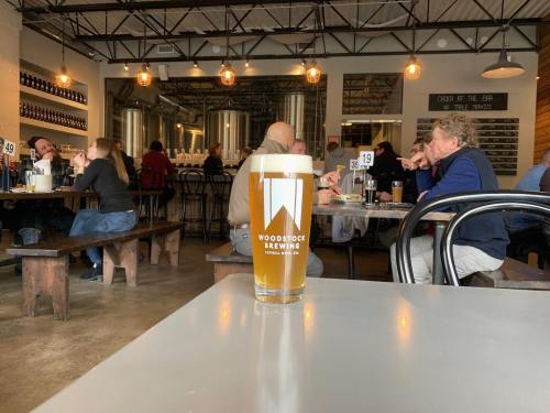 A glass of beer sits on a table in a bustling brewery with patrons enjoying food and drinks in the background.