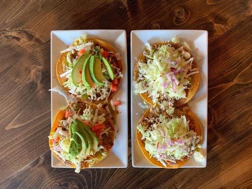 Two plates of tacos topped with avocado, cabbage, tomatoes, and cheese, served on a wooden table.