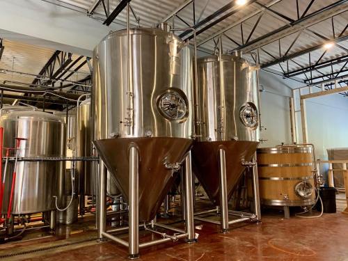 Two large stainless steel fermentation tanks and a wooden barrel in a brewery setting.