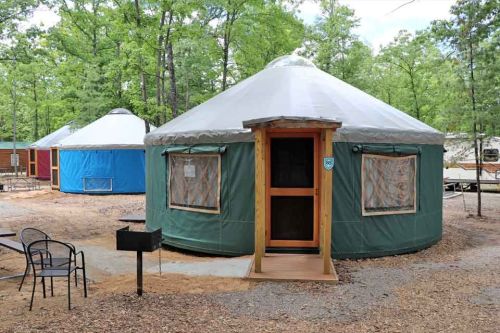 Two colorful yurts in a wooded area, with a picnic table and grill nearby.